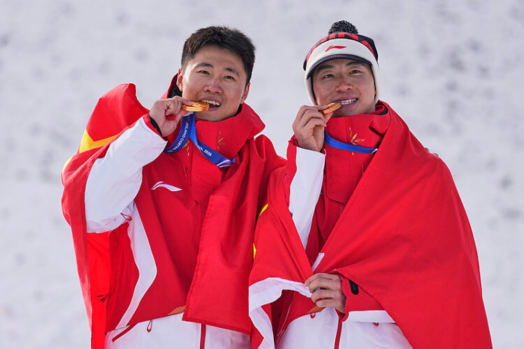 Olympics Gold medalist China's Wang Xindi, left, and bronze medalist China's Li Tianma bite their medals as they celebrate after the men's freestyle skiing aerials finals at the 2026 Winter Olympics, in Livigno, Italy, Friday, Feb. 20, 2026. (AP Photo/Abbie Parr)