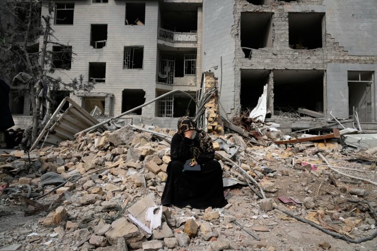 A woman sits on rubble across from a residential building damaged last Monday during the U.S.-Israeli air campaign in Tehran, Iran, Thursday, March 12, 2026. (AP Photo/Vahid Salemi)